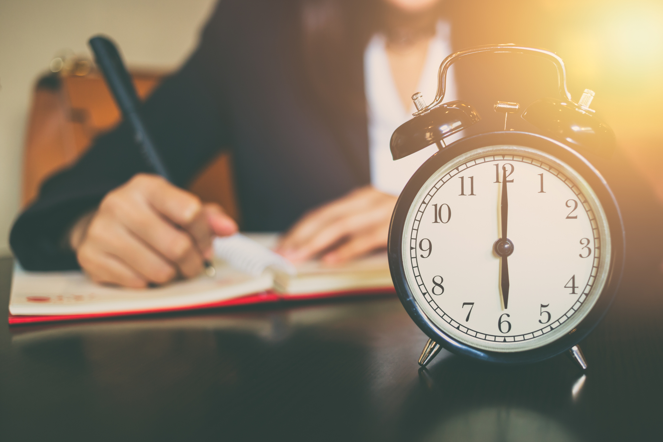 Traditional alarm clock with person writing in notebook behind it.